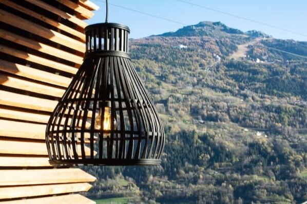 A black metal lantern hanging outdoors with a view of a mountainous landscape in the background.
