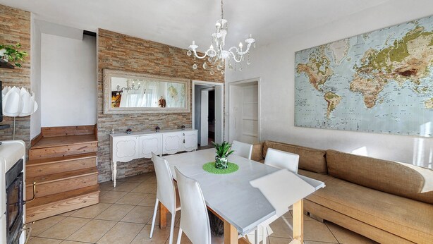 Una cocina moderna con una escalera de madera, un comedor con mesa y sillas blancas, un gran mapa mundial en la pared y una araña.