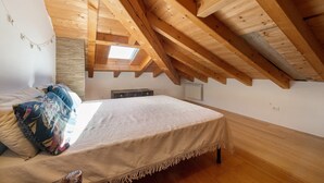 Un dormitorio con techo de madera inclinado, una cama con colcha estampada, una mesita y un radiador.