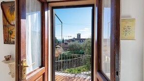 Puerta de madera abierta que da a un balcón con vistas a casas y una torre a lo lejos.
