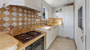 Una cocina con estufa a gas, armarios blancos, ventana y salpicadero de azulejos.