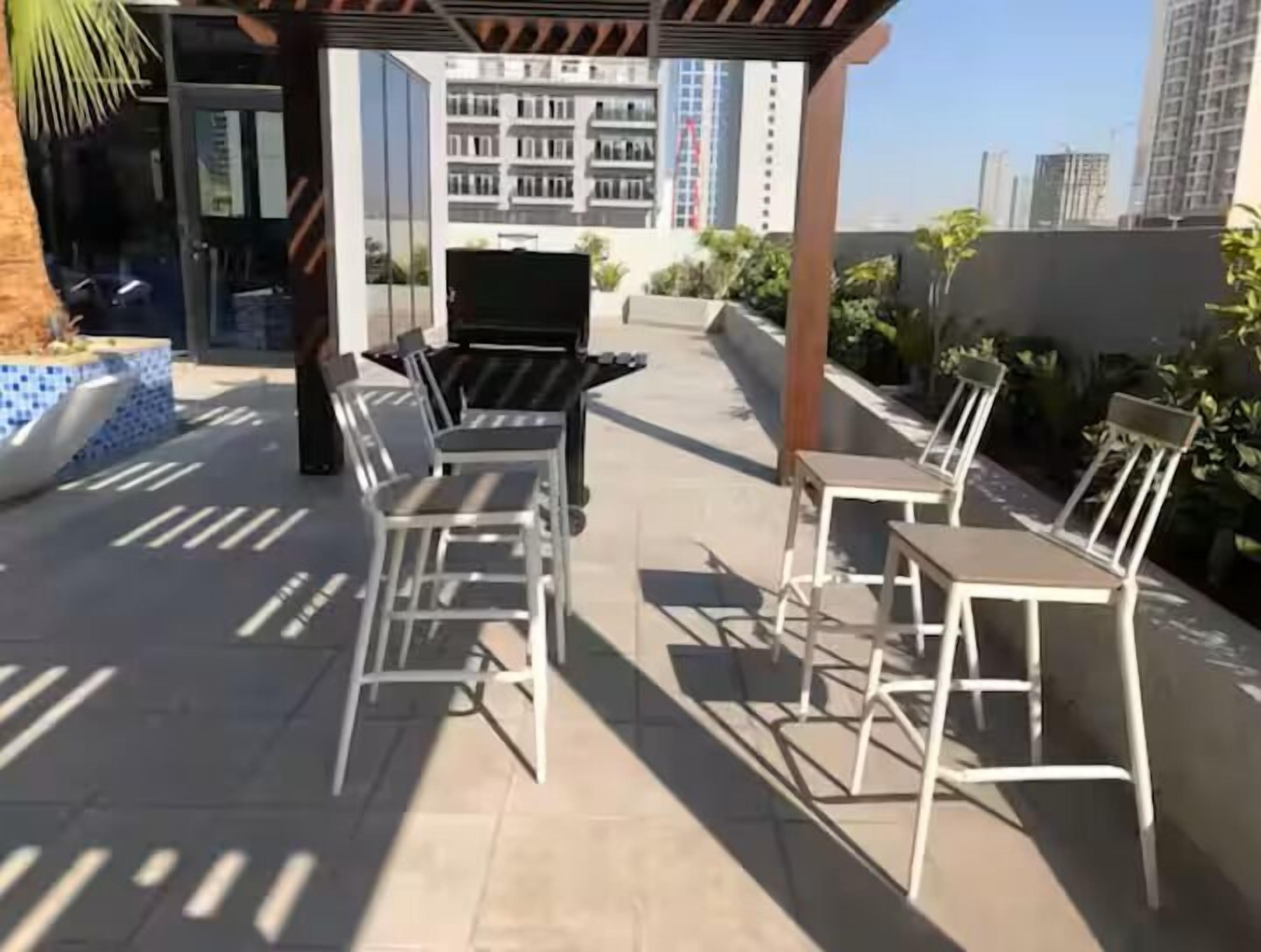Eine Terrass mit Grill, Stühlen und Tischen, umgeben von Pflanzen und Blick auf die Stadt.