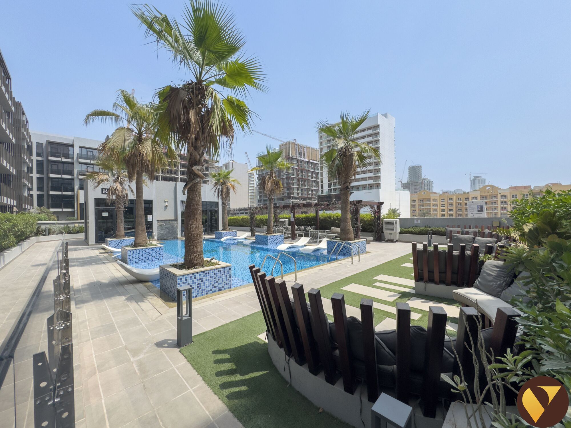 A rooftop pool area with palm trees, lounge chairs, and a view of surrounding buildings.