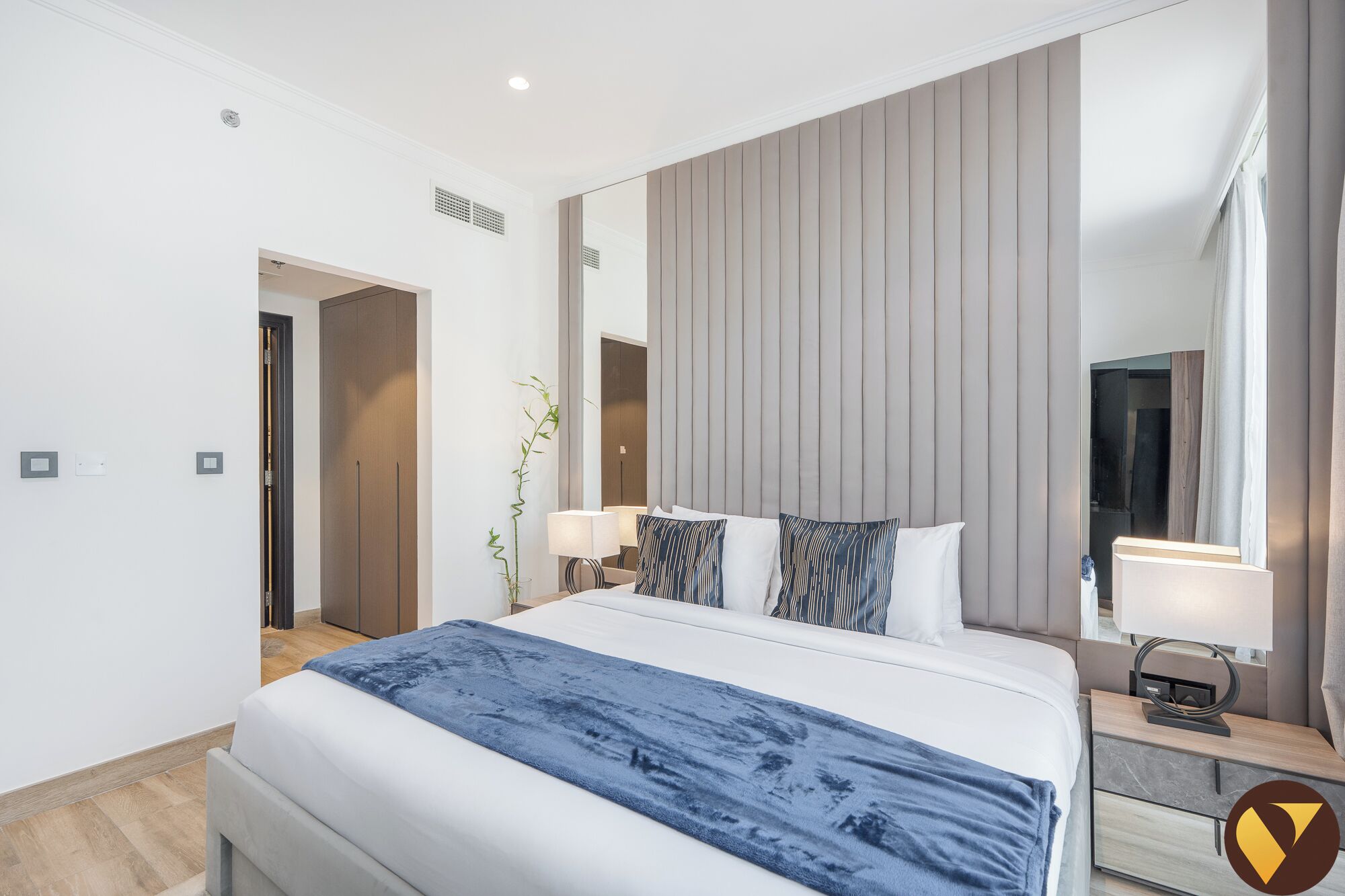 Ett modernt hotellrum med en stor säng, sängbord, en spegel och en växt.