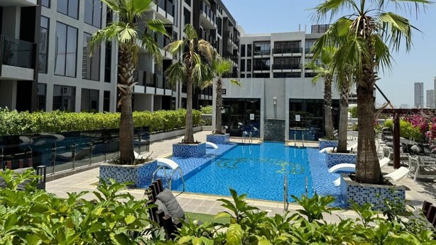 A modern building with a swimming pool, palm trees, and outdoor seating. - Vogue | Chaimaa Avenue JVC near Circle Mall (Dubai)