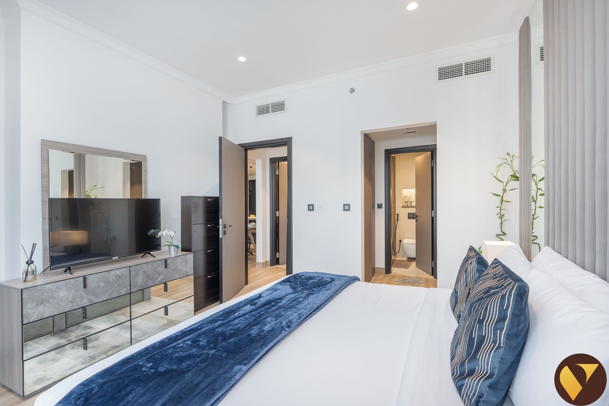 A modern bedroom with a large bed, a TV, a dresser, and two doors leading to other rooms.