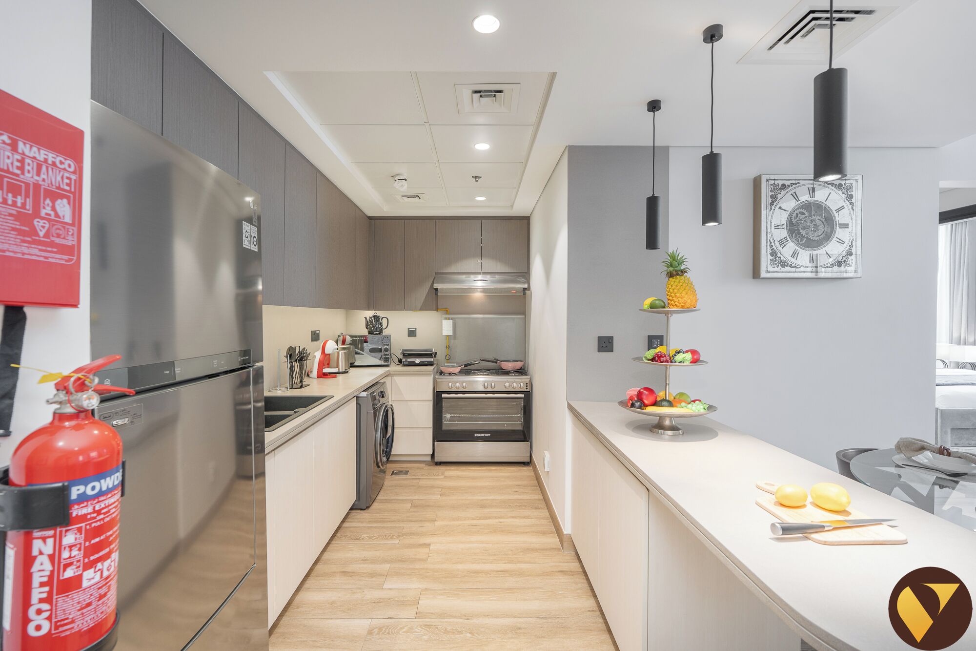 A modern kitchen with stainless steel appliances, a wooden floor, and a fruit display.