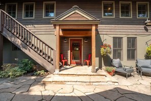 A two-story house with a stone staircase, a front porch with red chairs, and a hanging flower basket. - Coal Creek Hideaway (Crested Butte)