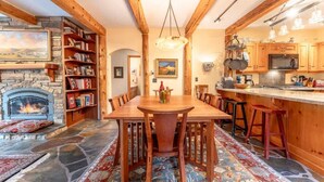 Un intérieur chaleureux avec une cheminée en pierre, une table à manger en bois et un coin cuisine.
