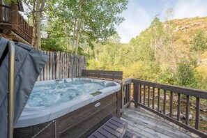 Ein Whirlpool auf einer Holzterrasse mit Blick auf einen bewaldeten Hang.