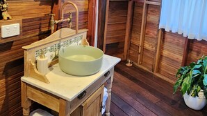 A rustic wooden bathroom with a large oval mirror, a wooden sink with a green basin, and a potted plant.