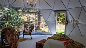 A tented accommodation with a bed, a chair, a table, and a chandelier.