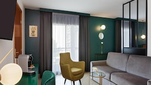 Un salon moderne avec un canapé, un fauteuil vert, une petite table et une machine à café.