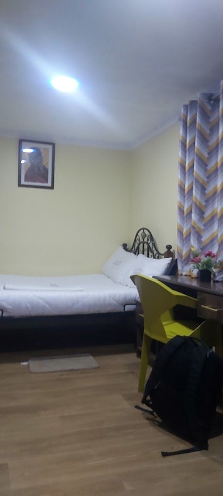 Een kleine kamer met een bed, een bureau, een stoel en een ingelijst beeld aan de muur.