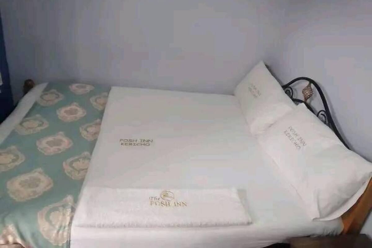 Ein Bett mit einem blumengemusterten Überwurf, ein weißes Kopfkissen mit dem Schriftzug 'The FOSH INN' und eine passende Kopfhaube.