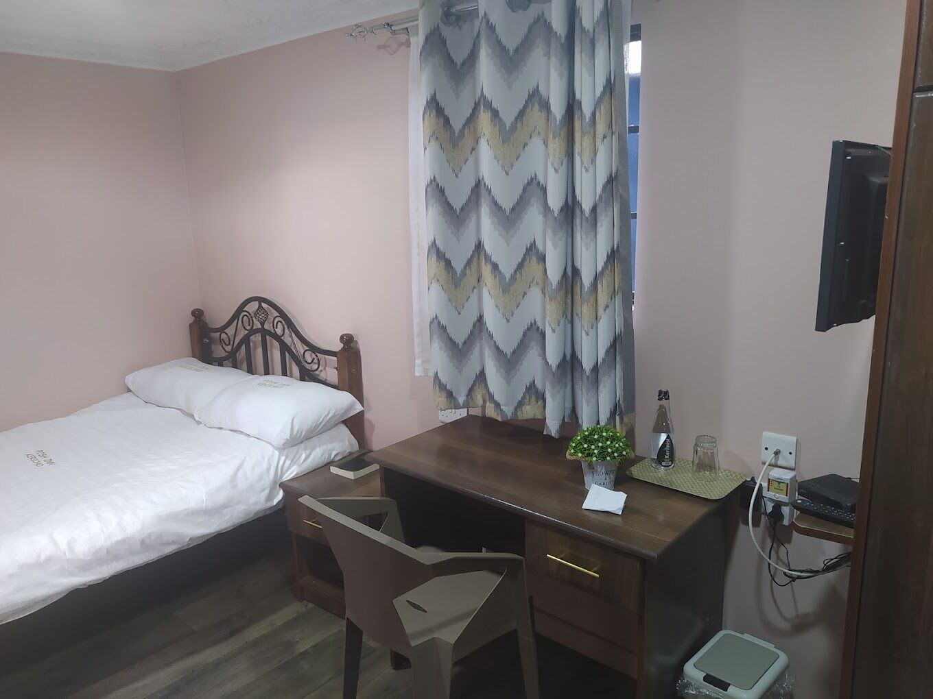 Ein kleines, ordentlich eingerichtetes Schlafzimmer mit einem Einzelbett, einem Holztisch, einem Stuhl und einem kleinen Tisch.