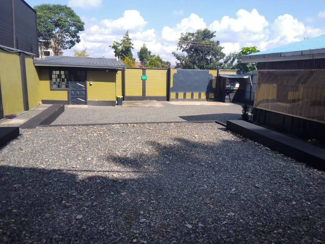 A gravel parking area with a building featuring a yellow facade and a black gate.