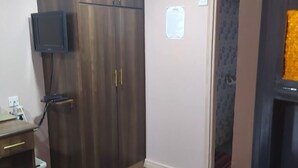 Ein Zimmer mit einem Holzkleiderschrank, einem Schreibtisch mit Computer und einem an der Wand montierten Fernseher.