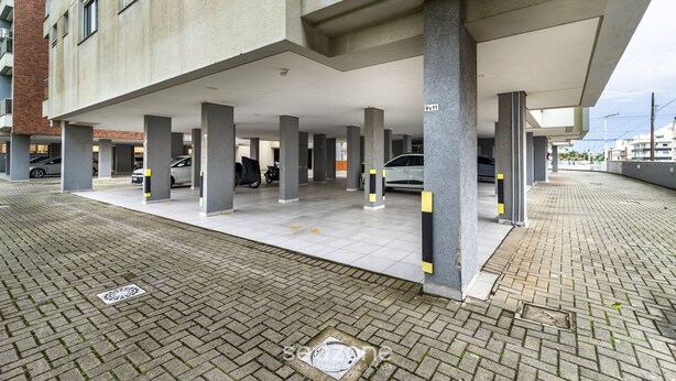 A covered parking area with concrete pillars and a tiled floor. - Building With Pool and gym in Floripa - RGN (Florianópolis)