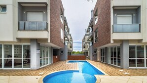 A swimming pool surrounded by modern buildings with balconies and large windows. - Building With Pool and gym in Floripa - RGN (Florianópolis)