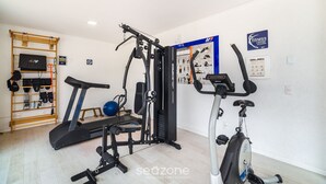 A home gym with a treadmill, elliptical, and weight machine. - Building With Pool and gym in Floripa - RGN (Florianópolis)