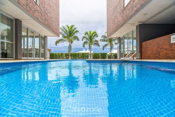 Piscina con agua azul cristalina, rodeada de paredes de vidrio y palmeras.
