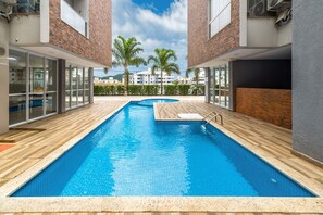 Una piscina con plataforma de madera, rodeada por puertas de vidrio y paredes de ladrillo.