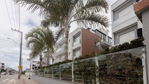 A modern urban street with residential buildings, a pedestrian crossing sign, and a glass fence with greenery. - Building With Pool and gym in Floripa - RGN (Florianópolis)
