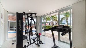 A gym with a treadmill, weight machines, and a view of a pool and buildings outside. - Building With Pool and gym in Floripa - RGN (Florianópolis)