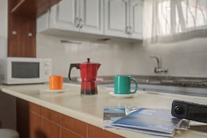 A kitchen counter with a microwave, a red coffee pot, and two cups.