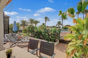 An outdoor seating area with lounge chairs and a table, surrounded by lush greenery and palm trees. - Holiday Apartment 'Los Porches K29' with Shared Pool, Private Terrace & Wi-Fi (Playa del Inglés)