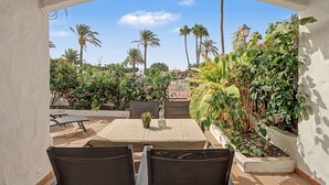 Ein Außenbereich mit Terrasse, Tisch und Stühlen, umgeben von üppiger tropischer Vegetation und Palmen.
