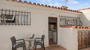 Eine Terrasse im Freien mit Tisch und Stühlen, eine Tür, die zu einer Küche führt, und ein Ziegeldach.