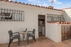 Um pátio externo com mesa e cadeiras, uma porta que dá para uma cozinha, e um telhado com azulejos.