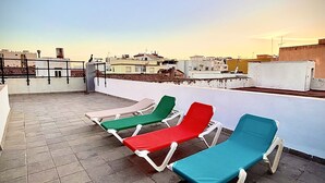 A rooftop terrace with four lounge chairs and a pool.