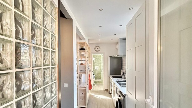 A narrow hallway with a wooden floor, a glass door on the right, and a closet with shelves on the left.
