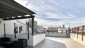 A rooftop terrace with tiled flooring, outdoor seating, and a pergola structure.