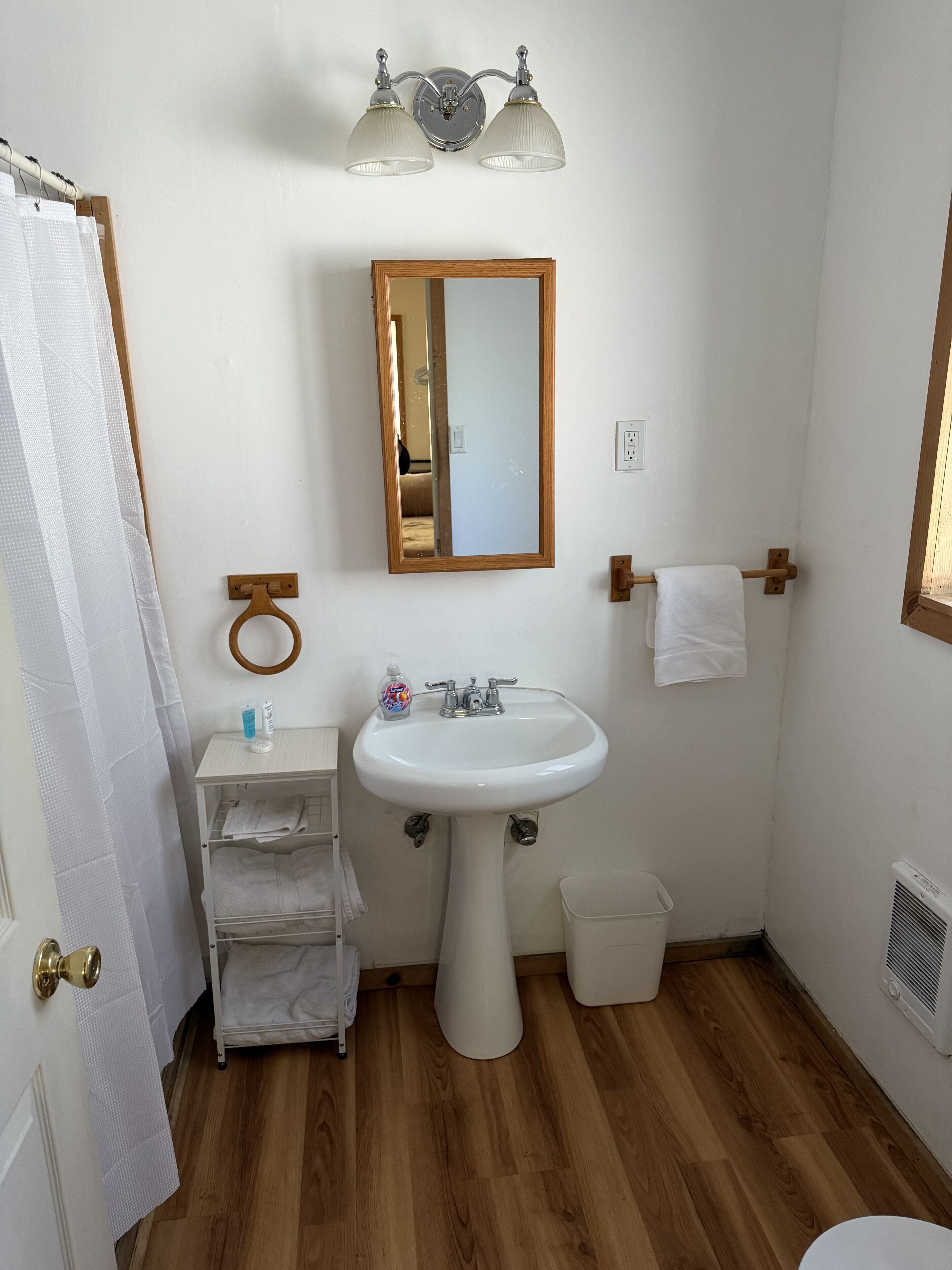 Een badkamer met een witte wastafel, een spiegel, een handdoekhouder, een douchegordijn en een klein plankje met toiletartikelen.