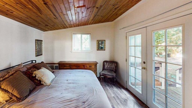 Un dormitorio con techo de madera, una cama grande, una silla y un ventanal corredero que da a un espacio exterior.