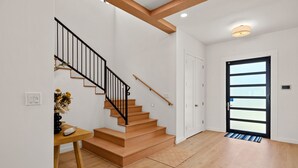 A modern interior with a wooden staircase, a door with a glass panel, and a small table with a vase. - Miramar House, 120 E. Constellation 6 Bedroom Home (South Padre Island)