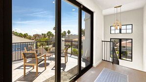 A balcony with a view of a residential area, a dining table with chairs, and a hanging light fixture. - Miramar House, 120 E. Constellation 6 Bedroom Home (South Padre Island)