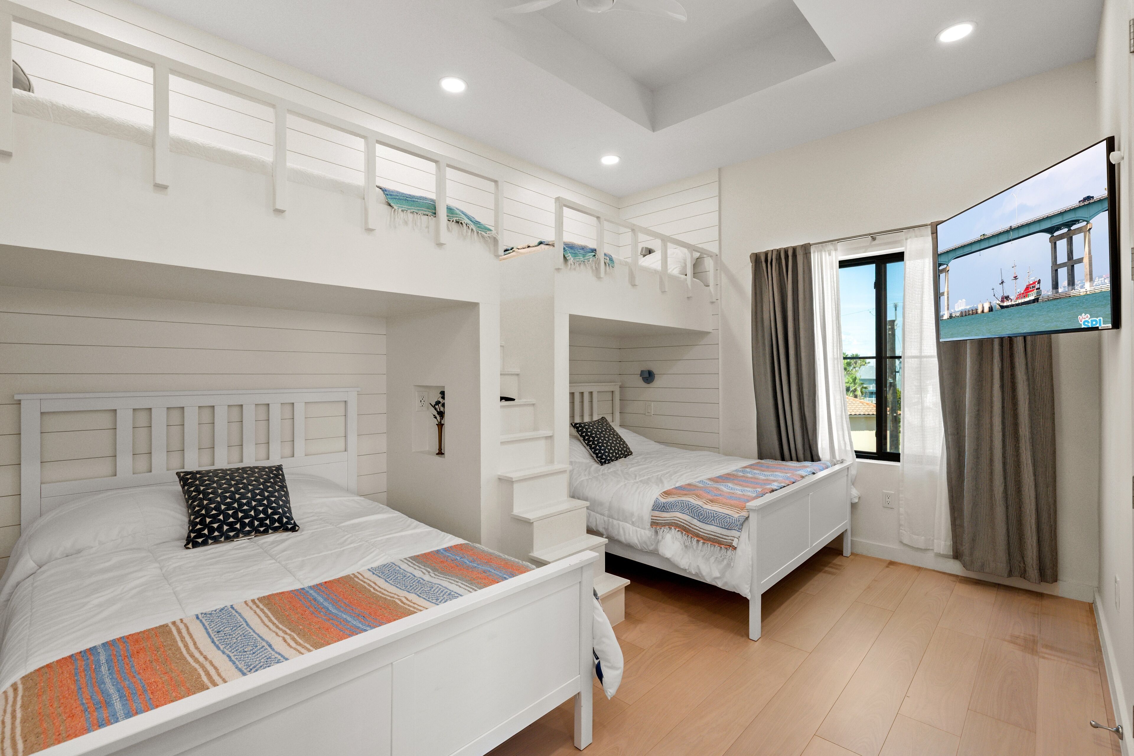 Un dormitorio con literas, televisión y ventana con cortinas.