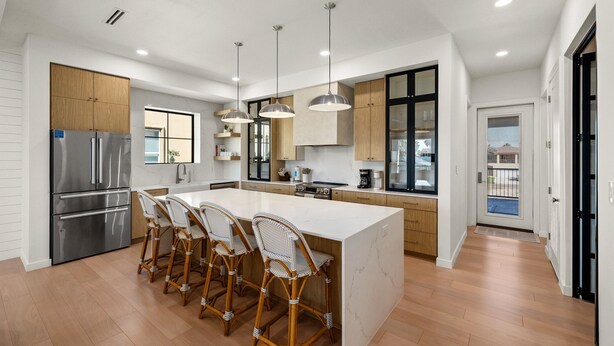 A modern kitchen with a central island, stainless steel appliances, and wicker bar stools. - Miramar House, 120 E. Constellation 6 Bedroom Home (South Padre Island)
