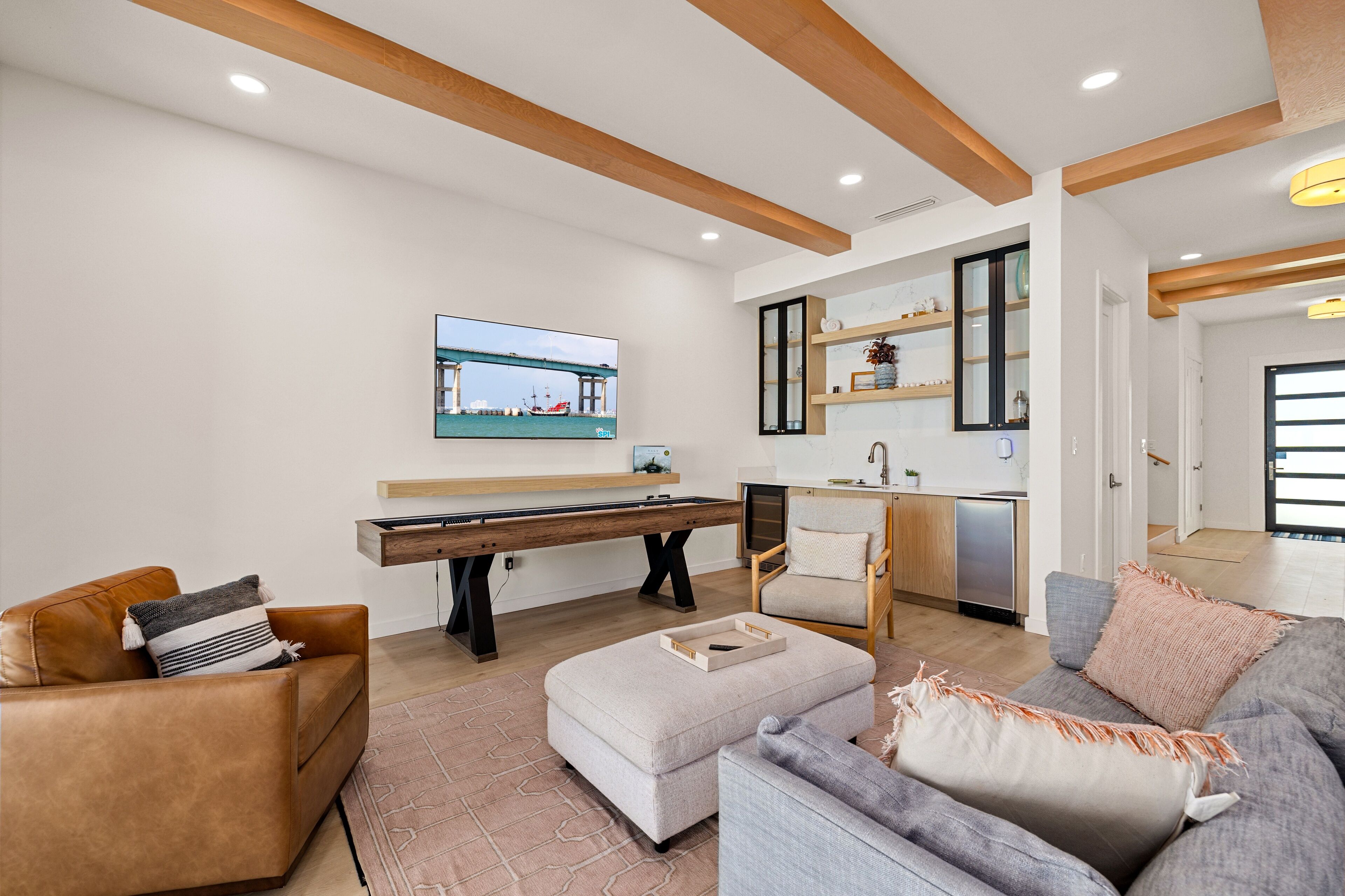A modern living room with a pool table, a sofa, and a television displaying a bridge scene.