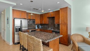 A modern kitchen with wooden cabinets, stainless steel appliances, and a granite island. - Sapphire Condo & Spa Unit # 406 3 Bedroom Condo (South Padre Island)
