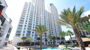 A high-rise hotel with a pool area, palm trees, and lounge chairs. - Sapphire Condo & Spa Unit # 406 3 Bedroom Condo (South Padre Island)