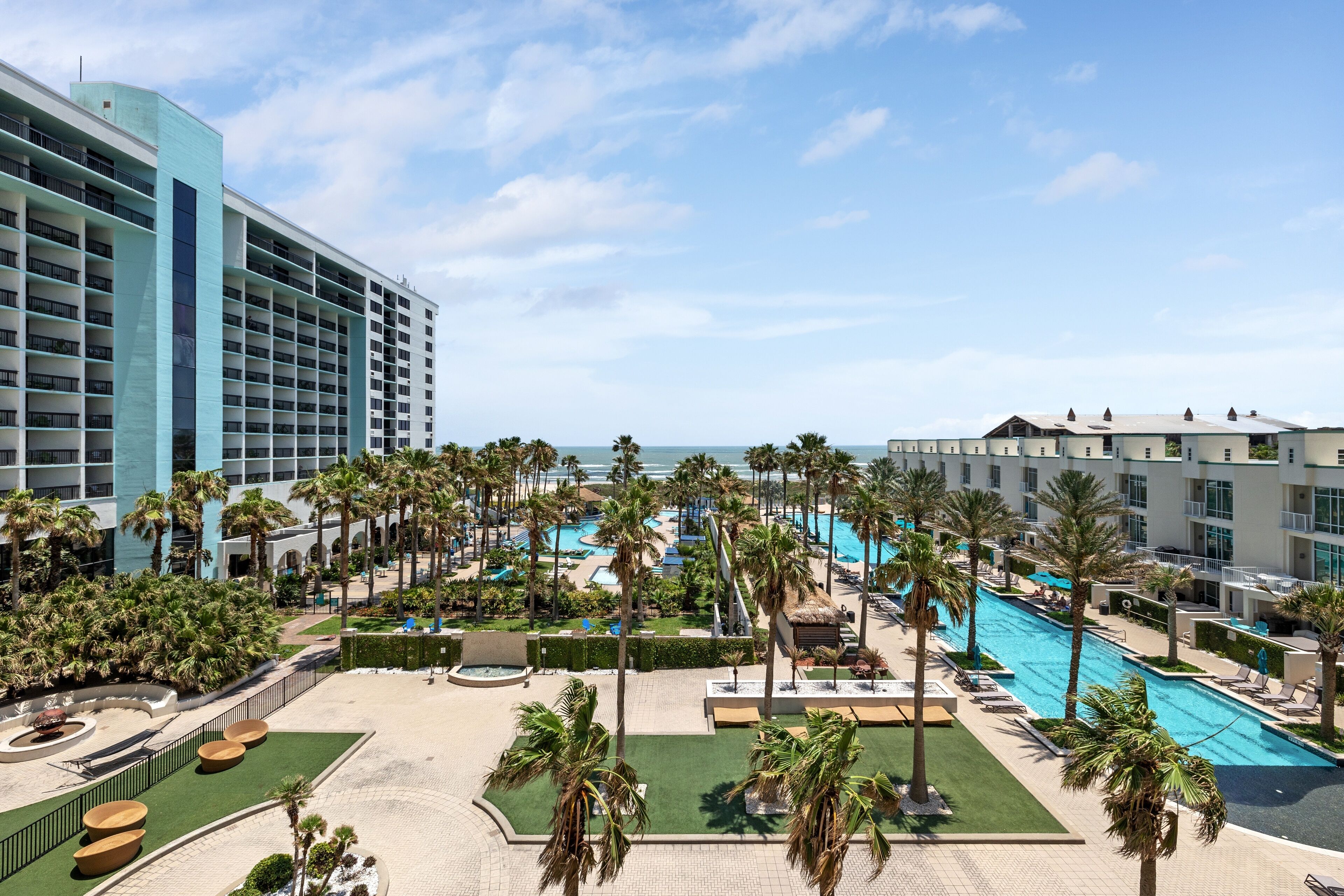 Un hotel con un amplio espacio de piscina, palmeras y vista al océano.