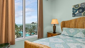 A hotel room with a large window, a bed with patterned bedding, a nightstand with a lamp, and a woven headboard. - Sapphire Condo & Spa Unit # 406 3 Bedroom Condo (South Padre Island)