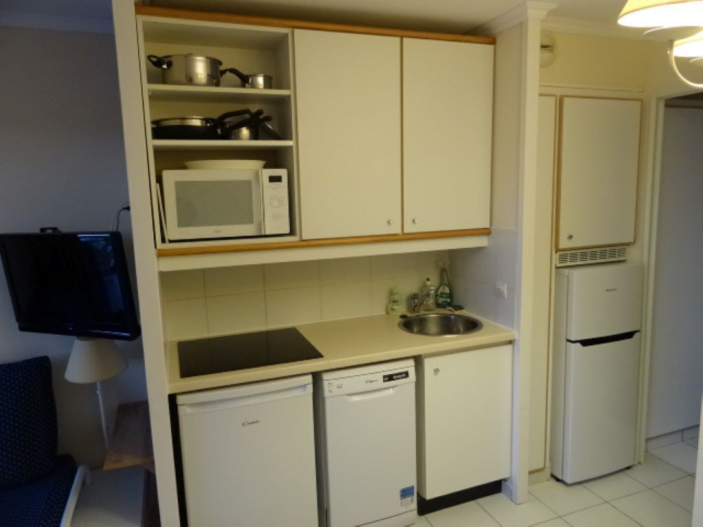 Une cuisine de taille réduite, avec des meubles blancs, un four à micro-ondes, un évier, un lave-vaisselle et un réfrigérateur.