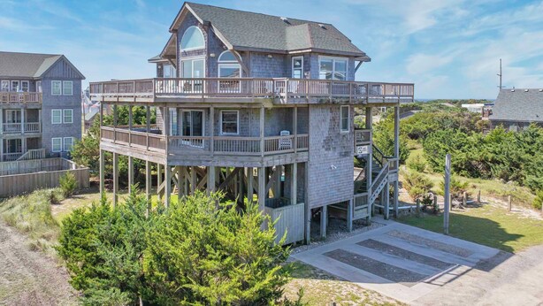 A multi-story house with a balcony on the second floor, a covered deck area, and a view of the surrounding landscape. - Oceanside, Dog-Friendly Home in Rodanthe with Private Pool and Hot Tub (Rodanthe)